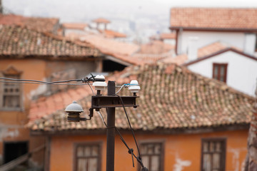 Old electric linear insulator on pole and old style Turkish homes in background