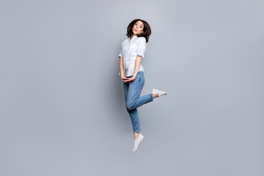 Full length, fullbody portrait of pretty, girlish coquette, charming, modern, stylish girl in denim outfit, pants, jumping in the air with raised leg, looking at camera, isolated on grey background