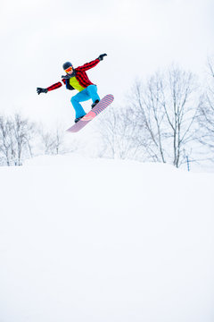 Photo of sportive man in helmet with snowboard jumping in snowy resort