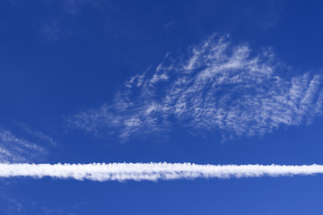 Skyscape: Cloudscape with a large contrail in front of higher thin and wispy cirrus clouds over...