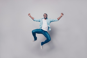 Fototapeta na wymiar Full length, size portrait of confident attractive, joyful, cheerful, positive, glad guy in shirt, sneakers jumping with raised fists, looking at camera, isolated on grey background