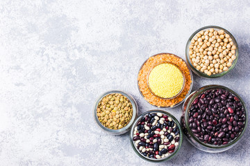 Various dry legumes in glass jars on stone background. Top view, space for text.
