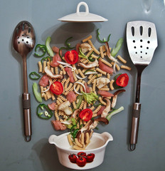 still life of products: pasta, vegetables, pans with lids and cooks, on a glass table