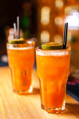 Close-up of two colorful orange cocktails with lime and brown sugar in bar, blurred background.