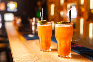 Close-up of two colorful orange cocktails with lime and brown sugar in bar, blurred background.