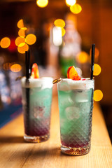Two blue cocktails with lemon on the bar, blurred background.