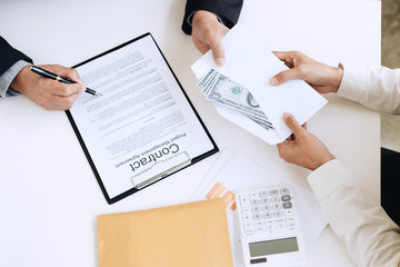 Bribery and corruption concept, bribe in the form of dollar bills, Businessman giving money in the envelope while making deal to agreement a real estate contract and financial corporate