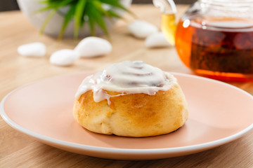 Freshly baked cinnabon roll with sweet glaze on pink plate with tea on background