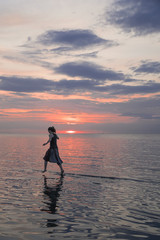 Frau läuft durch das Meer in den Sonnenuntergang hinein