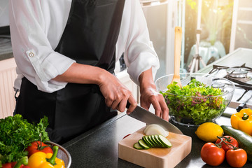 Close up of woman hand cutting onion on chopping wood board with sharp knife and cooking vegetables salad in kitchen