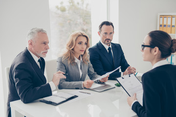 Portrait of young attractive woman in glasses having job interview with three stylish business...
