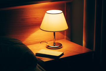 Book and vintage lamp on night table in hotel room
