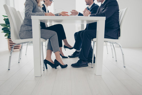 Side view, cropped, bottom view portrait of stylish, attractive, classy business people's legs under table, in suits, sitting in work place, station, having conference, consulting, clients, brokers