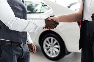 Handshake closeup of African men with the girl in the showroom on the background of a new car
