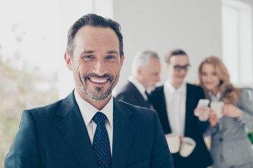 Close up portrait of attractive, elegant, smart brunet director in classic tuxedo with tie, looking at camera, colleagues drinking coffee, talking, speaking on blurred background