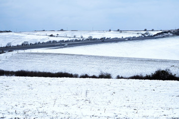 Sussex downs rolling hills and meadows a hillside in winter covered with a thin layer of snow running through the middle is a road with traffic on it