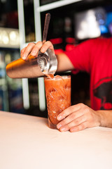 Close-up of expert bartender making orange cocktail in bar