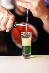 Close-up of expert bartender making shot cocktail on the white bar.