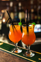 Two orange cocktails with green cherry on the bar