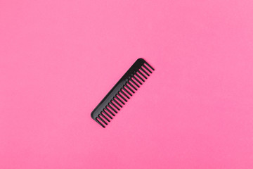 top view of one black comb, isolated on pink