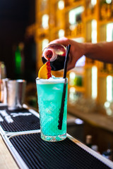 Close-up of expert bartender making blue, turquoise cocktail in bar