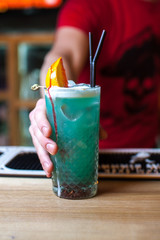 Bartender serving blue cocktail with lemon and streaks of syrup in bar