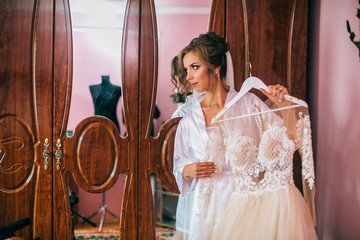 The charming bride stands near wedding dress