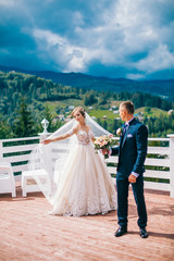 a loving couple - the bride and groom on a walk in the mountains, embrace, beautiful spring green landscape. Kissing newlyweds bride and groom at mountains restaurant terrace.