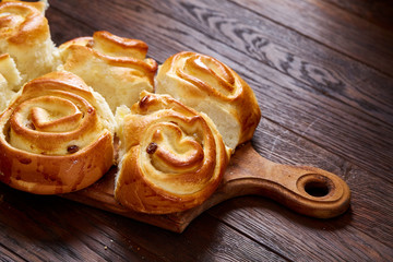 Homemade rose buns on wooden cutting board over rustic vintage background, close-up, shallow depth of field