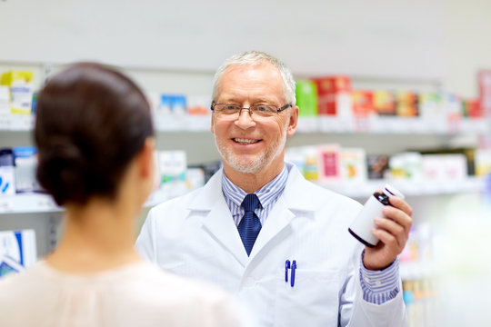 medicine, healthcare and people concept - senior apothecary with drug and female customer at pharmacy