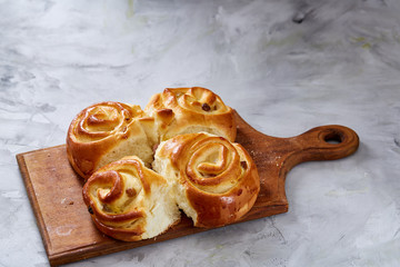 Homemade rose buns on wooden cutting board over white textured background, close-up, shallow depth of field
