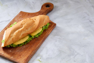 Fresh and tasty sandwich with cheese and vegetables on cutting board over white textured...