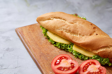 Fresh and tasty sandwich with cheese and vegetables on cutting board over white textured background, selective focus.