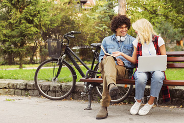 Young cheerful couple sitting on the bench studying together in the park