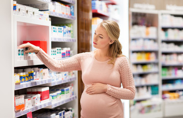 pregnancy, medicine, people, healthcare and expectation concept - happy pregnant woman looking for medication at pharmacy