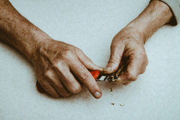 Elderly man sharpens pencil with clerical knife. Hands of old man close up.