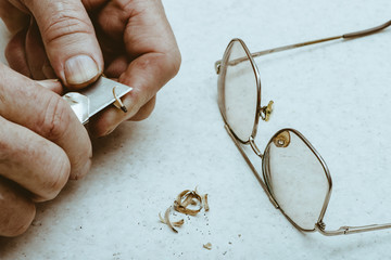 Elderly man sharpens pencil with clerical knife. Hands of artist close up. Shavings on table next...