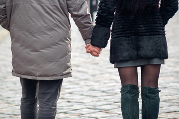 Love concept. Couple holding hands each other while going for a walk in winter street, view from back