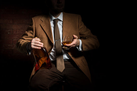 Man in suit with cognac glass and bottle in luxury interior. without face