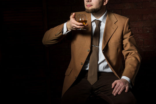 Man in suit with cognac glass in luxury interior. No face