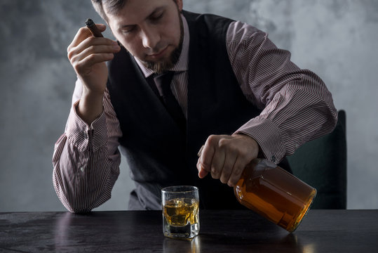 A man sits at a table and pours into a glass from a bottle of whiskey