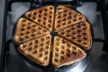 Just cooked, delicious, tasty, hot yogurt pancakes on waffle iron on fire stove in kitchen. Dinner is ready. Sweet golden brown waffles ready to be eaten