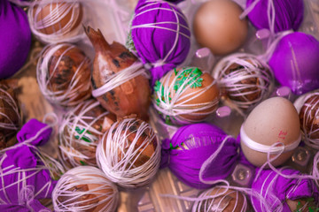 Easter eggs prepared for dyeing in onions peels, decorated with natural fresh leaves, plants, rice, colorful fabric and tied with white threads. Eggs laying in wicker wooden basket full of green grass