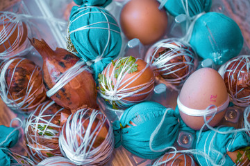 Easter eggs prepared for dyeing in onions peels, decorated with natural fresh leaves, plants, rice, colorful fabric and tied with white threads. Eggs laying in wicker wooden basket full of green grass