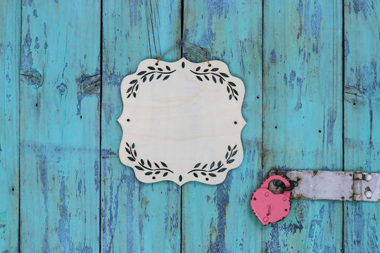 Blank wooden sign with floral border hanging on rustic antique teal blue wood door with heart-shaped lock