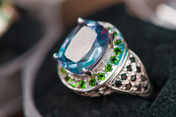 Macro shot of silver engagement ring in gift box on colorful, sparkling background. Ring made of sapphire, amethyst, chrome diopside stones. Healing, natural crystals and , powerful energy