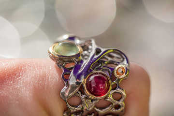 Macro shot of silver engagement ring on colorful, sparkling background. Wedding ring with prehnite stone, ruby and sapphire crystals. Royal, expensive and luxury gift