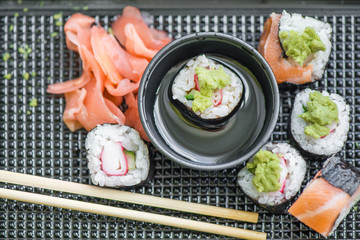 Fresh and delicious maki and nigiri sushi rolls with tiger shrimps, salmon, philadelphia cheese and wasabi served with soy sauce and ginger slices on black take away plate. Japanese food in restaurant