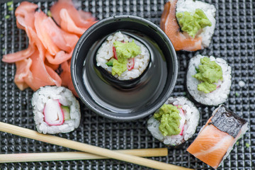 Fresh and delicious maki and nigiri sushi rolls with tiger shrimps, salmon, philadelphia cheese and wasabi served with soy sauce and ginger slices on black take away plate. Japanese food in restaurant