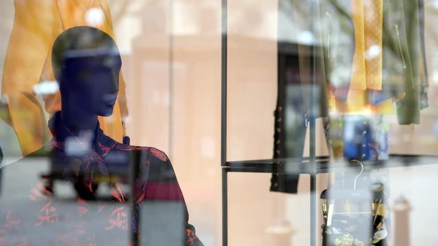 Black, female shop window mannequin looking out onto a busy street.